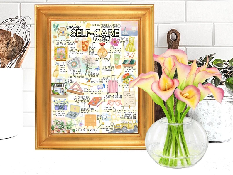May include: A framed print with a gold border displays a watercolour "Spring Self-Care Checklist." The print is next to a vase of pink calla lilies. The checklist includes ideas like "Open all your windows" and "Take a spring photo."