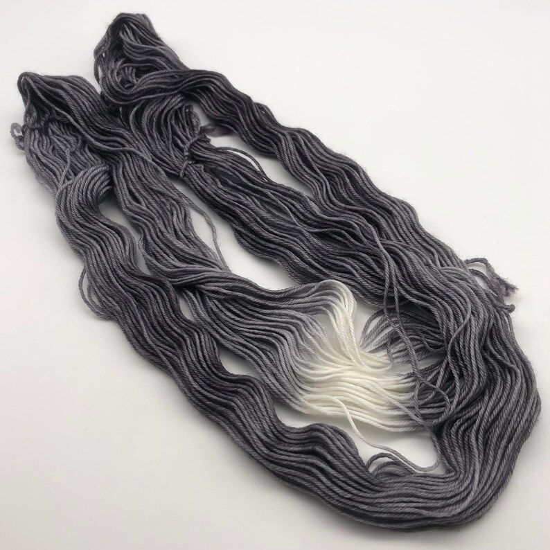 May include: Two skeins of yarn in a gradient colorway, starting with a dark gray and fading to white.