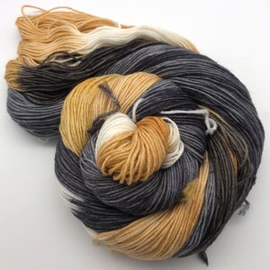 May include: A skein of yarn in a variegated colorway with shades of black, white, and beige.