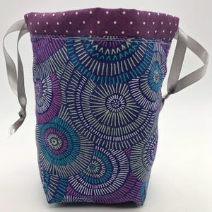 Può includere: Borsa a cordoncino viola con fodera a pois bianchi e un motivo geometrico colorato di cerchi e linee.
