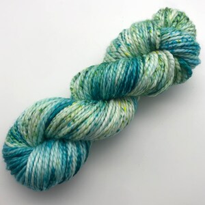 Könnte beinhalten: Eine Garnrolle in einer hellblauen, grünen und weißen Farbkombination mit gelben Sprenkeln. Das Garn besteht aus Baumwolle und ist perfekt zum Stricken oder Häkeln.
