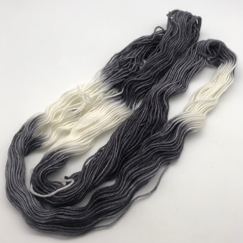 May include: A skein of yarn with a gradient color transition from white to dark gray.