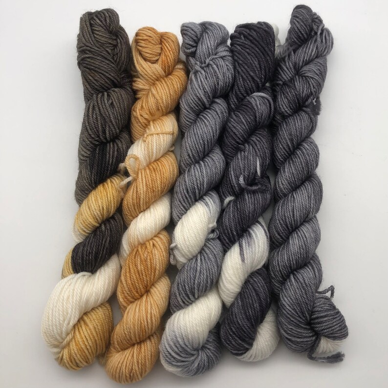 May include: Five skeins of yarn in different colors. Two skeins are a gradient of brown to white, two skeins are a gradient of gray to white, and one skein is a gradient of brown to gold.