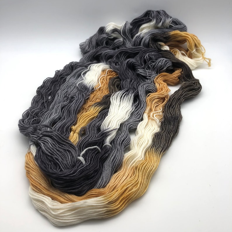 May include: A skein of yarn with a gradient of black, white, and gold colors.