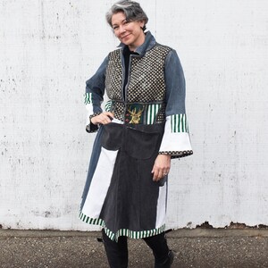 May include: A long denim coat with a patchwork design. The coat features a black and white skirt, a polka-dot bodice, and green and white striped accents on the sleeves. The coat is worn with black boots.