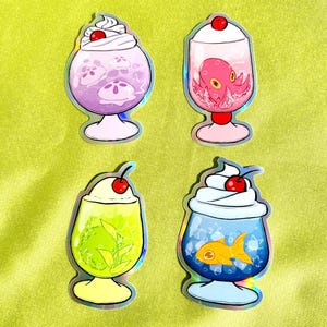May include: Four holographic stickers featuring stylized glass desserts. One contains purple jellyfish, one a pink octopus, one green leaves, and one a gold fish. Each glass is topped with white whipped cream and a bright red cherry on top.