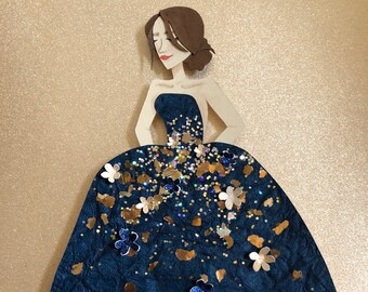 Può includere: Una bambola di carta che indossa un abito blu con dettagli di glitter dorati e argentati. L'abito ha una scollatura senza spalline e una gonna ampia.