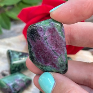 May include: A close-up of a green and pink zoisite crystal. The crystal is smooth and polished, with a variety of shades of green and pink.
