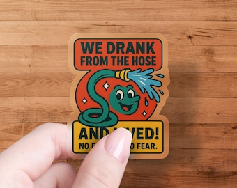 Op de afbeelding: Een sticker met een cartoon illustratie van een groene tuinslang met een lachend gezicht, die water spuit. De tekst luidt: "WE DRANK FROM THE HOSE AND LIVED! NO FEAR."