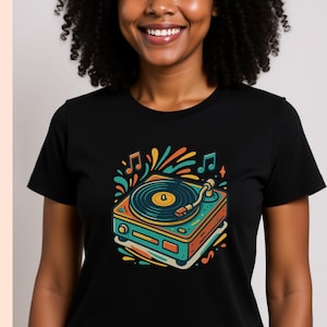 Puede incluir: Camiseta negra con una colorida ilustración de un tocadiscos retro. El diseño incluye notas musicales y salpicaduras de color vibrantes, creando un tema vintage y musical.