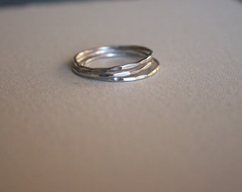 May include: A set of three thin, silver-colored stacking rings. Each ring features a hammered, textured surface that reflects light, creating a series of small, irregular facets along the circular bands. The rings are stacked together in a single pile.