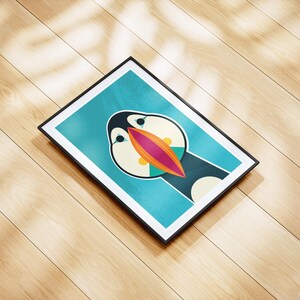 May include: A framed art print featuring a stylized illustration of a puffin bird. The artwork has a teal background with the puffin's face in the center, showcasing a large, colorful beak with orange, pink, and teal accents. The frame is black.