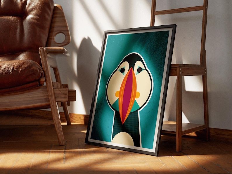 May include: Framed art print featuring a stylized illustration of a puffin bird. The artwork has a teal background with the puffin's face in cream, black, and orange. The bird's beak is a vibrant combination of red and orange.