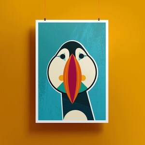 May include: A framed art print featuring a stylized illustration of a puffin. The bird has a black head, white cheeks, and a large, colorful beak with orange, red, and teal accents. The background is a textured teal color.