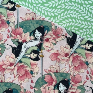 May include: Fabric featuring a repeating pattern of a woman in a traditional outfit, swords, and pink flowers on a light pink background. A section of green fabric with a white leaf pattern is in the upper right corner.