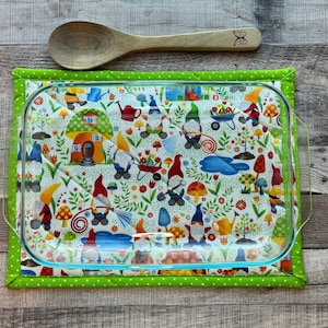 May include: A green and white quilted hot pad with a gnome pattern. The hot pad has a glass baking dish on top of it.
