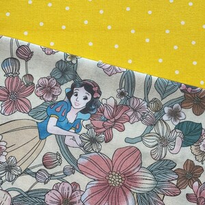 May include: A fabric design featuring a cartoon illustration of Snow White surrounded by pink and beige flowers. The design is set against a yellow background with white polka dots.