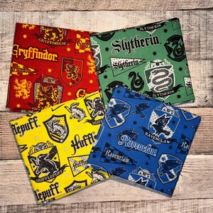 May include: Four fabric squares with Harry Potter house crests: Gryffindor in red, Slytherin in green, Hufflepuff in yellow, and Ravenclaw in blue. Each square features house colors, crests, and text on a wooden background.