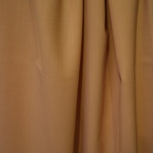 May include: A close-up of a smooth, light brown fabric with a subtle texture. The fabric is draped in soft folds, creating a luxurious and elegant look.