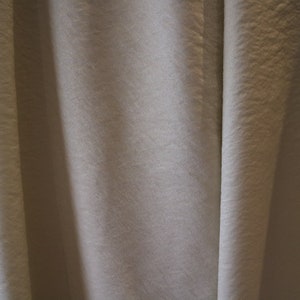 Könnte beinhalten: Nahaufnahme eines glatten, gebrochenweißen Stoffes mit einer dezenten Textur. Der Stoff ist so gefaltet, dass eine Reihe vertikaler Linien entsteht.