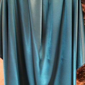 May include: A teal blue satin fabric with a smooth, silky texture. The fabric is draped and folded, showcasing its luxurious feel.