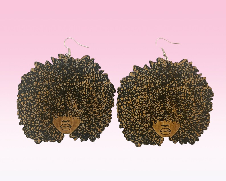 May include: A pair of wooden earrings featuring a black silhouette of a woman with an afro hairstyle. The earrings are brown and have a silver hook.