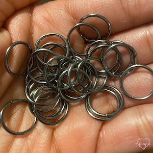 May include: A pile of black metal jump rings. The rings are all the same size and are arranged in a random pattern.
