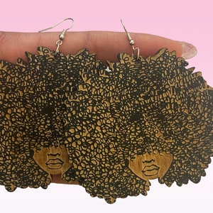 May include: A pair of wooden earrings featuring a black and brown silhouette of a woman with an afro hairstyle.