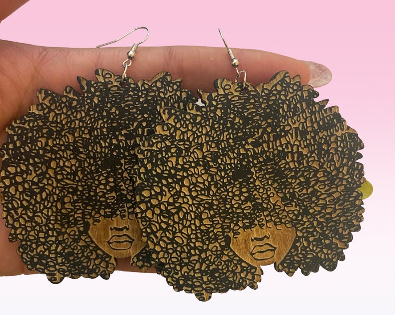 May include: A pair of wooden earrings featuring a black and brown silhouette of a woman with an afro hairstyle.
