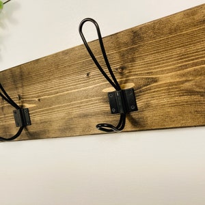 May include: A rustic wooden coat rack with two black metal hooks. The wood is stained a dark brown, showcasing the natural grain. The hooks are mounted on black metal plates, creating a contrast against the wood. Perfect for entryways or bedrooms.
