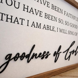 May include: A wooden framed sign with the words "YOU HAVE BEEN FAITHFUL" and "goodness of God" in black lettering. The background is white with a wood grain texture. The frame is a dark brown color.