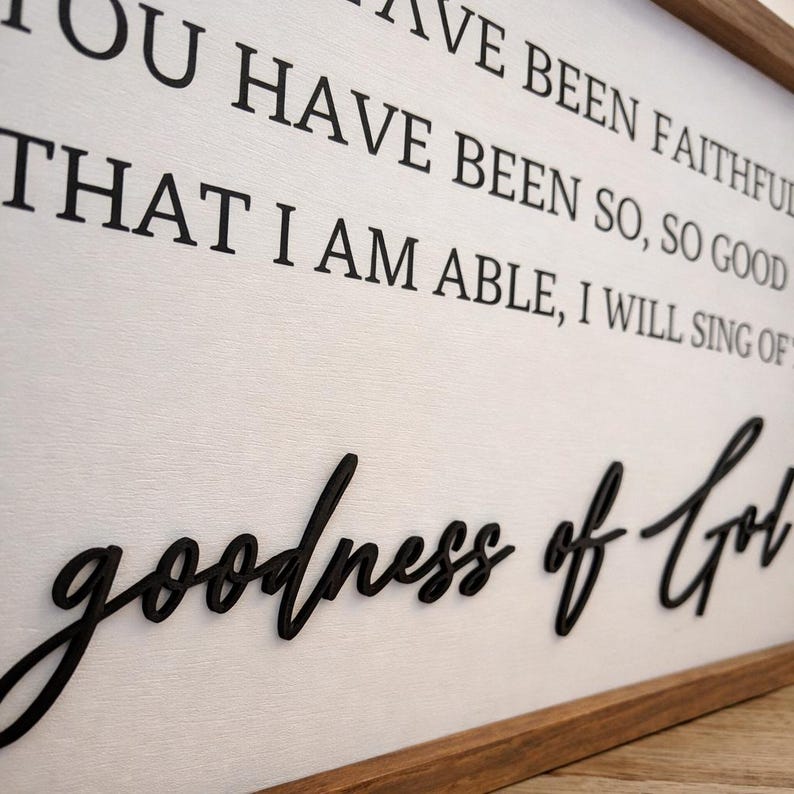 May include: A wooden framed sign with the words "YOU HAVE BEEN FAITHFUL" and "goodness of God" in black lettering. The background is white with a wood grain texture. The frame is a dark brown color.