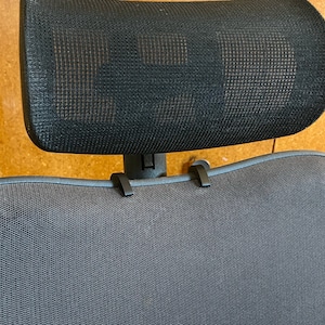May include: A black mesh headrest with two black clips attached to the back of a gray mesh office chair.
