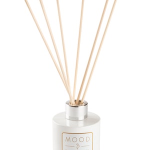Op de afbeelding: Witte keramische diffuserfles met een zilveren deksel en houten stokjes. De fles heeft de tekst "MOOD & MOOD" in goud gedrukt.