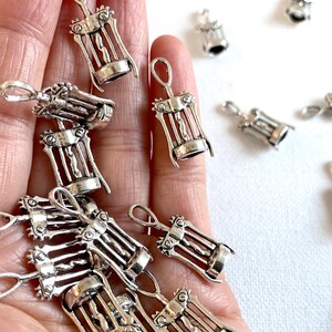 K&ouml;nnte beinhalten: Nahaufnahme einer Hand, die einen Haufen silberfarbener Korkenzieher-Anh&auml;nger h&auml;lt. Die Anh&auml;nger sind detailliert und haben einen Vintage-Look.