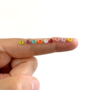 Può includere: Una fila di 12 piccoli bottoni a due fori in vari colori, tra cui giallo, verde, viola, blu, arancione, bianco, rosso, rosa e lavanda.