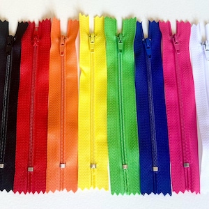 Peut inclure: Une collection de fermetures éclair colorées, allant du noir au blanc, en passant par le rouge, l'orange, le jaune, le vert, le bleu et le rose. Chaque fermeture est ouverte, révélant les dents et le curseur métallique. Idéal pour la couture et les travaux manuels.