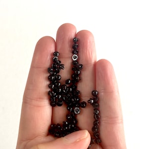 May include: A hand holding a large quantity of black plastic snap fasteners. The fasteners are small and round with a metal center.