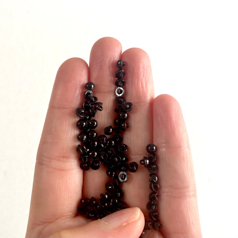 May include: A hand holding a large quantity of black plastic snap fasteners. The fasteners are small and round with a metal center.