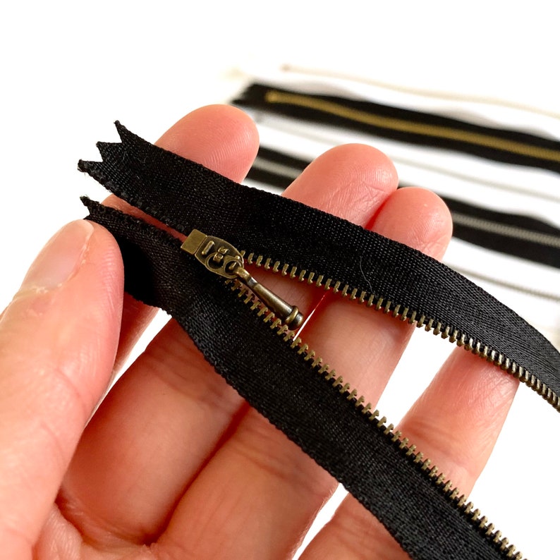 May include: A black zipper with a brass slider and teeth. The zipper is open and the slider is pulled back.