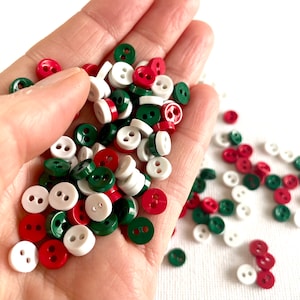May include: A collection of small, two-hole buttons in red, white, and green. The buttons are scattered on a white surface.
