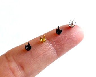 May include: Four metal studs in different colors: gold, black, silver, and black. The studs have a pointed top and a flat base.