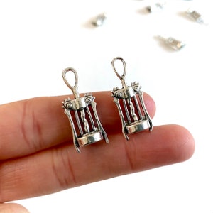 K&ouml;nnte beinhalten: Zwei silberfarbene Korkenzieher-Anh&auml;nger, jeweils mit einem detaillierten Design, werden auf einem Finger gezeigt. Die Anh&auml;nger sind etwa 2,5 cm lang.