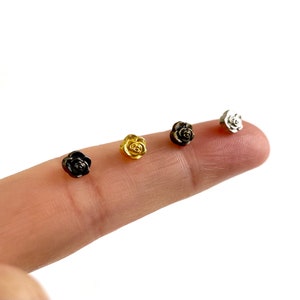 May include: Four small rose-shaped metal charms in gold, silver, black, and bronze.