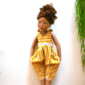 May include: A doll with brown curly hair wearing a yellow and white striped jumpsuit with a colorful bunting trim.