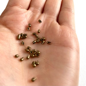 Könnte beinhalten: Nahaufnahme einer Hand, die einen Haufen kleiner, goldfarbener Metalltacker mit einer spitzen Spitze und einer kleinen Schlaufe oben hält.
