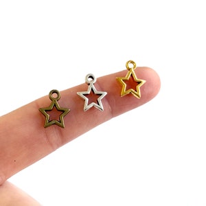 May include: Three star-shaped metal charms with a hole at the top for attaching to jewelry or other crafts. The charms are in gold, silver, and bronze.
