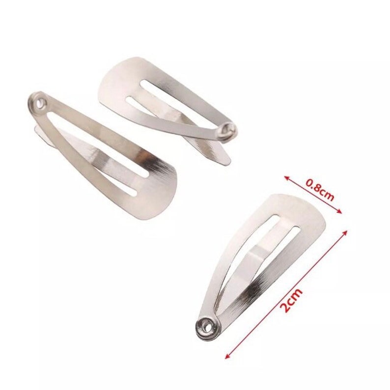 Op de afbeelding: Drie zilverkleurige metalen haarspeldjes. Elk speldje is ongeveer 0,8 cm breed en 2 cm lang. De speldjes hebben een eenvoudig ontwerp met een gleuf in het midden en een scharnierende sluiting.
