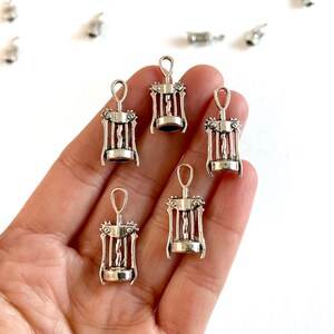 K&ouml;nnte beinhalten: Sechs silberfarbene Korkenzieher-Anh&auml;nger aus Metall. Die Anh&auml;nger haben die Form eines traditionellen Korkenziehers mit einer Spirale und einem Griff. Die Anh&auml;nger befinden sich auf einer Hand.
