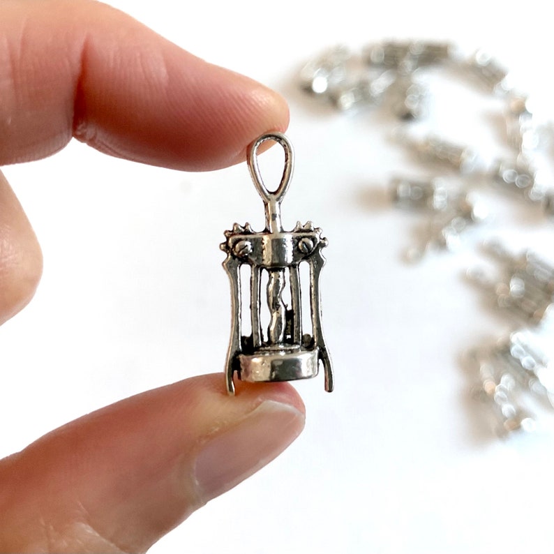 K&ouml;nnte beinhalten: Ein silberfarbener Metall-Korkenzieher-Anh&auml;nger. Der Anh&auml;nger ist in Form eines traditionellen Korkenziehers mit einem Griff und einer Spirale geformt.